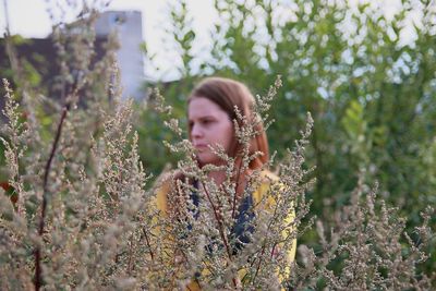 Woman looking away while standing by plant