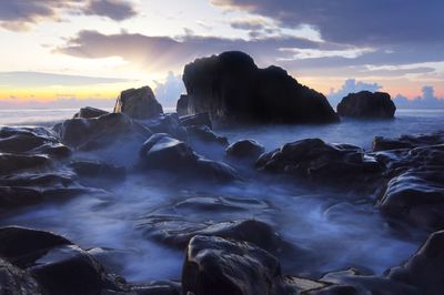 Rocks in sea against sky during sunset