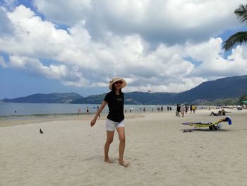 Woman walking at beach against cloudy sky