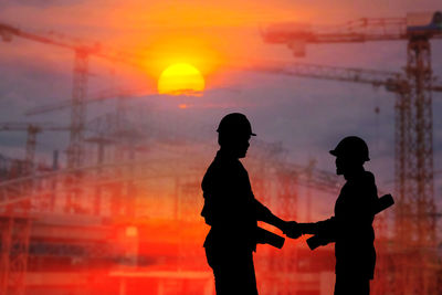 Silhouette man standing against buildings during sunset