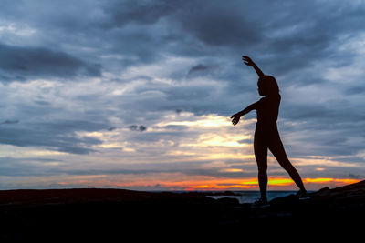 Silhouette woman dancing on land against sky during sunset