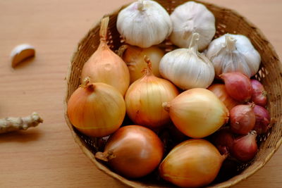 Close-up of onions and garlic bulbs in wicker basket on table