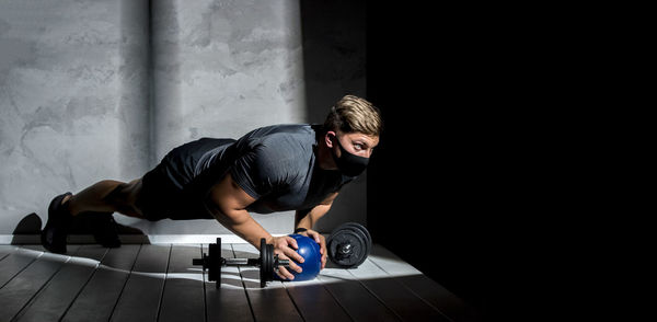 Full length of young man wearing mask exercising in darkroom