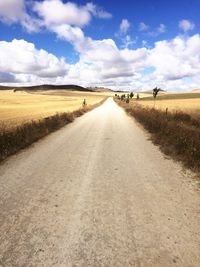 Road passing through field against cloudy sky