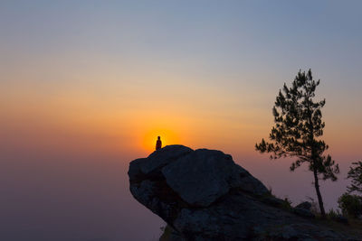 Silhouette woman on rock formation against sky during sunset