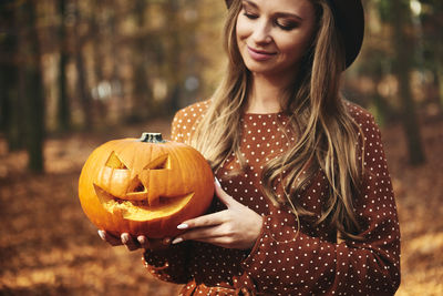 Portrait of smiling woman holding pumpkin at night during halloween