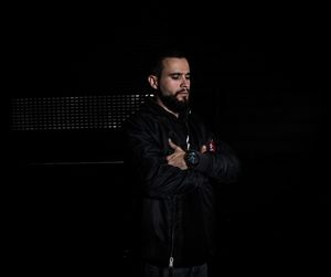 Young man with arms crossed standing against black background