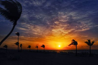 Silhouette people on beach against dramatic sky during sunset