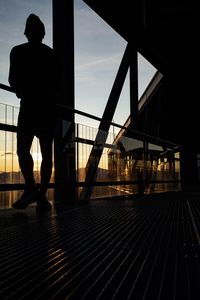 Silhouette man walking on bridge against sky during sunset