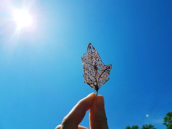 Close-up of hand holding umbrella against blue sky