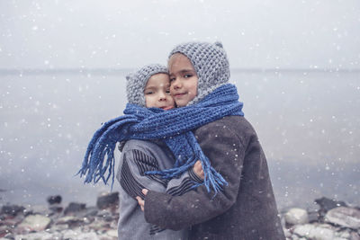 Girl in knitted grey hat hugging her frozen smaller brother, one scarf for two to keep warm