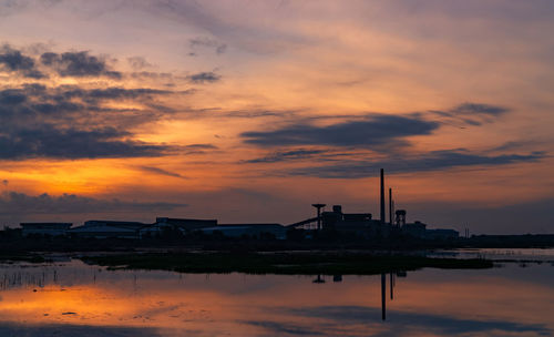 Landscape of factory industry buildings with dark blue and orange sunset sky reflection on water.