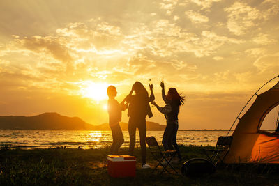 People standing on beach against sky during sunset