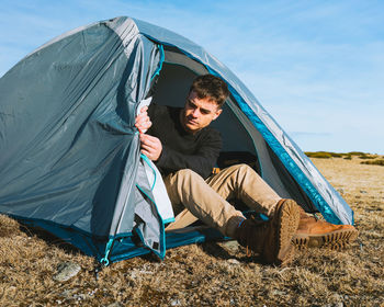 Side view of man sitting at tent against sky