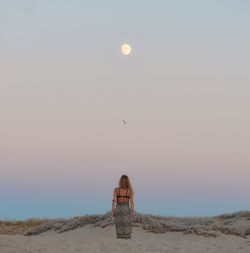 Woman standing on land against sky during sunset