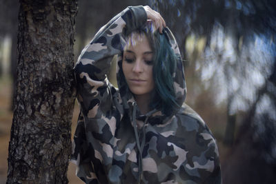 Portrait of young woman standing by tree trunk