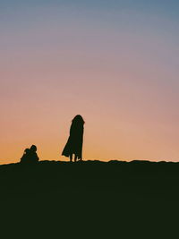 Silhouette people standing on land against clear sky during sunset
