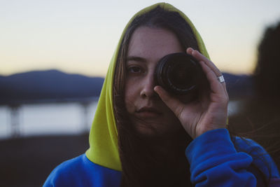 Portrait of young woman photographing against sky