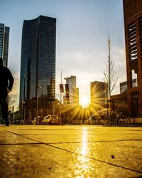 City street by buildings against sky during sunset