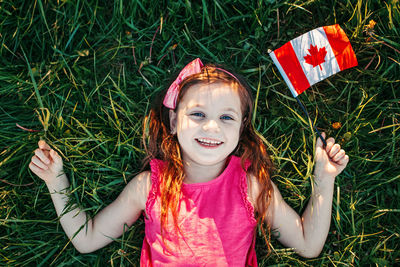Happy girl with canadian flag lying on field