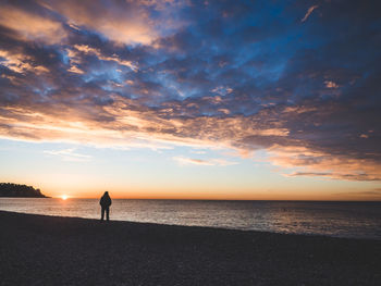 Silhouette man standing on beach against sky during sunset