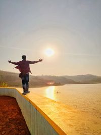 Full length rear view of man standing on lake against sky
