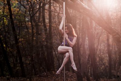 Woman dancing on pole against trees in forest