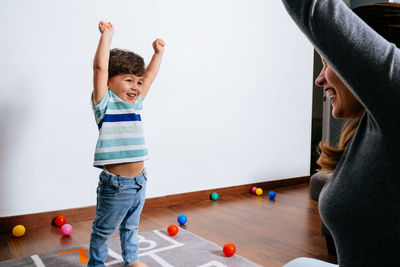 Delighted lady and cute toddler raising arms and celebrating victory while playing games on floor at home