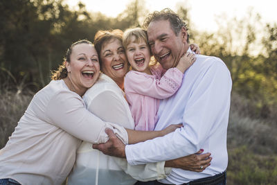 Multigenerational family embracing and laughing in field  person