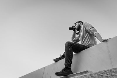 Low angle view of woman photographing against clear sky