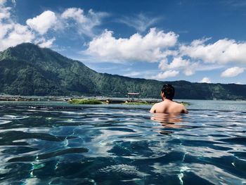 Rear view of shirtless man in infinity pool by lake