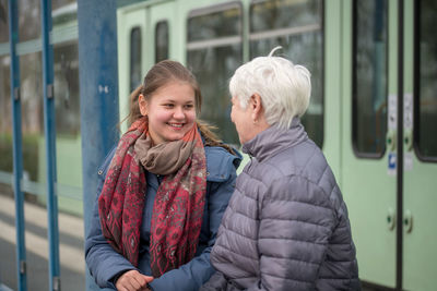 Smiling grandmother and granddaughter sitting at railroad station platform