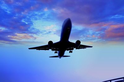 Low angle view of airplane flying against sky at sunset