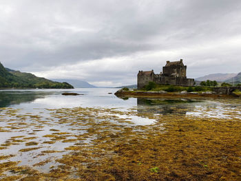 Buildings by sea against cloudy sky