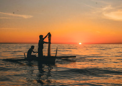 Silhouette woman standing in sea against sky during sunset