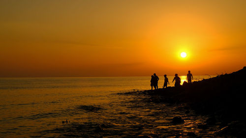 Silhouette people on beach against orange sky