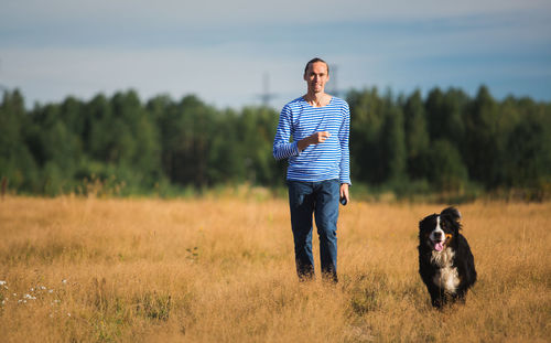 Portrait of man with dog standing on grassy land