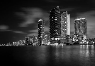 Illuminated modern buildings in city against sky at night