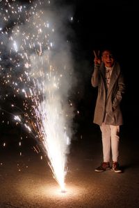 Full length of man standing by illuminated firework against sky at night