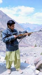 Young man with rifle against mountains