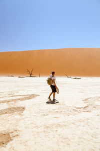 Full length of man walking in desert against clear blue sky