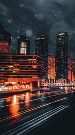 Light trails on road against illuminated buildings in city at night