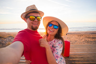 Portrait of smiling young couple on beach against sky