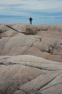 Man standing on rock by sea against sky