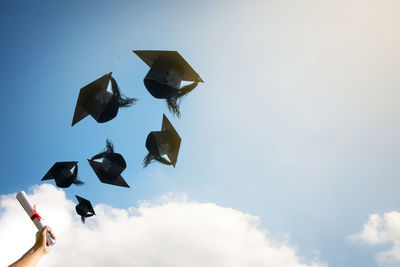 Low angle view of cropped hand with certificate against mortarboards in mid-air