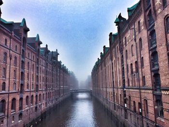 Canal amidst buildings in city against sky