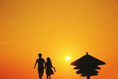 Silhouette men standing against orange sky