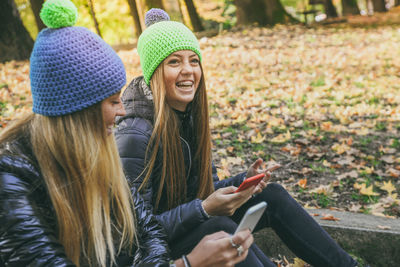 Smiling girls sitting in the park using smartphone. teen using mobile phone sisters chat with friend