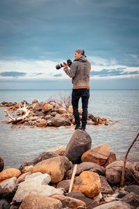Full length of man photographing on rock at beach against sky
