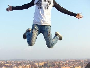 Low angle view of man jumping in city against sky